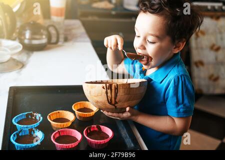A little boy licks a spoon with chocolate dough Stock Photo