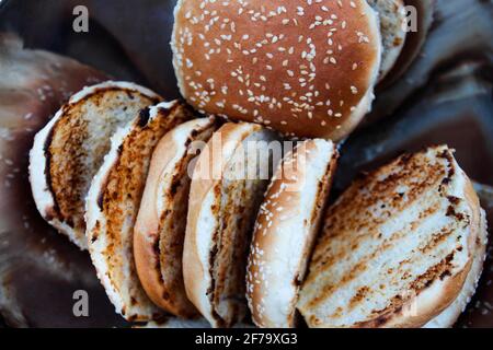 Grilled hamburger buns with sesame seeds in a metal bowl. Stock Photo