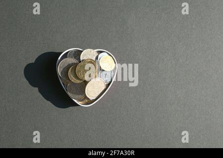 Coins in heart shaped container. Love for money concept. Top view with copy space. Stock Photo