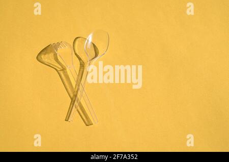 Transparent spoon and fork cutlery with shadows, on yellow background. Plastic pollution or waste concept. Stock Photo