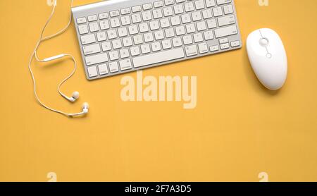 Top view of white keyboard, mouse and earphones on yellow background table. Copy space. Stock Photo