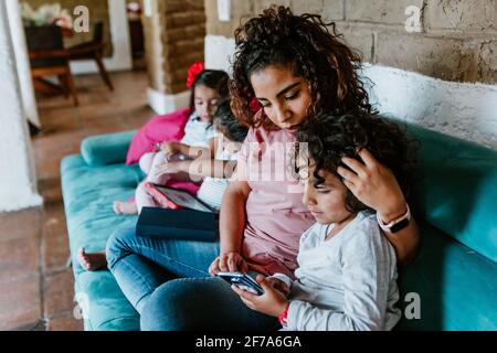 latin mother on sofa at home with little boy child use phone browse Internet together in Mexico city Stock Photo