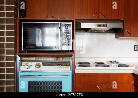 A 1960s Moffat 69 wall oven, 1980s Panasonic Dimension 3 microwave/convection oven and Moffat 40 built-in stovetop inside a retro kitchen. Stock Photo