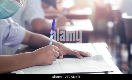 Students taking exam and writing answer in classroom with wear face mack. Education test concept Stock Photo