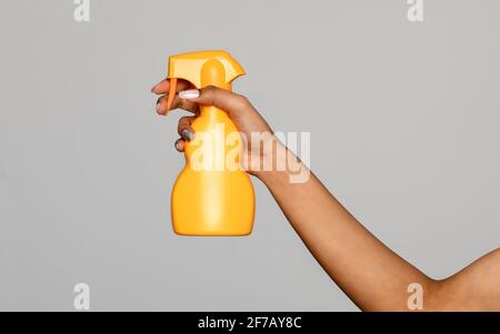 Hand of a black woman holding an unlabelled generic yellow plastic spray bottle pointing to the side over a grey studio background for advertising Stock Photo