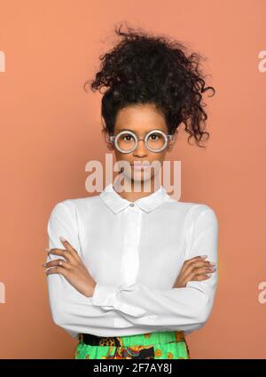 Serious confident black woman with her long curly hat tied to the top of her head standing wearing round eyeglasses staring at the camera over a studi Stock Photo