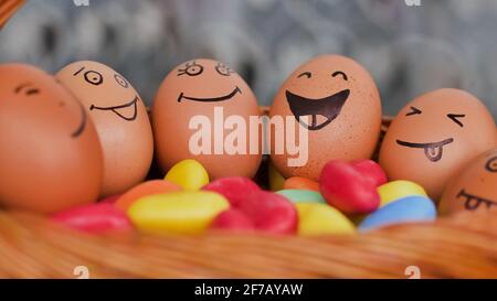 Stack of eggs with hand drawn faces on straw basket with colorful candy, easter preparation, holiday mood concepts Stock Photo