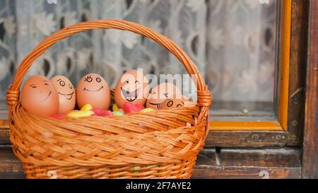 Stack of eggs with hand drawn faces on straw basket with colorful candy, easter preparation, holiday mood concepts Stock Photo