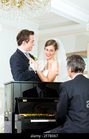 Bridal couple in front of a piano, the pianist is playing a waltz Stock Photo