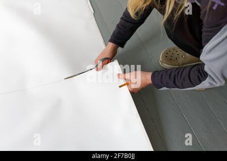 A female artist cutting canvas to prepare her own picture supports. Stock Photo