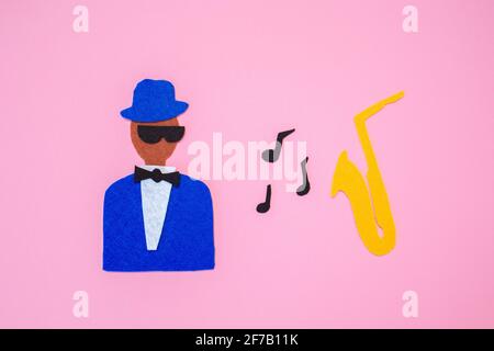 World Jazz Day. Silhouette of a musician with a saxophone on a pink background, cutted out of felt. Flat lay. Stock Photo