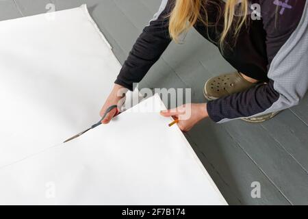 A female artist cutting canvas to prepare her own picture supports. Stock Photo