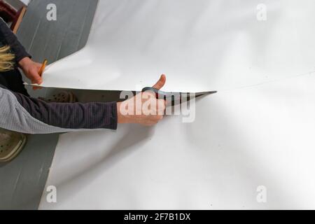 A female artist cutting canvas to prepare her own picture supports. Stock Photo