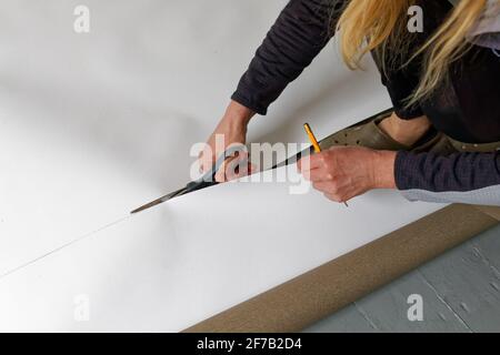 A female artist cutting canvas to prepare her own picture supports. Stock Photo