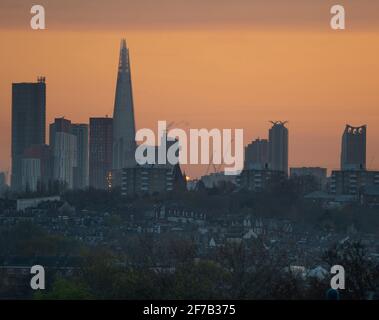 6 April 2021. Orange sky at sunrise behind The Shard skyscraper with low rise suburbs in the foreground, view from Wimbledon Hill Stock Photo