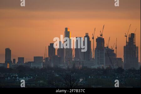 6 April 2021. Orange sky at sunrise behind City of London skyscrapers and The Shard with low rise suburbs in the foreground, view from Wimbledon Hill Stock Photo