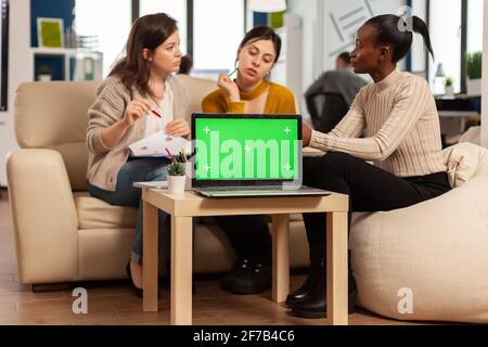 Laptop with chroma key display on table in startup business workplace. African manager discussing talking project statistics with employees on modren office sitting on couch. Stock Photo