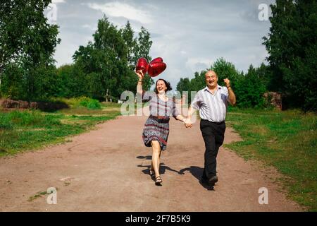 Russia Vyborg 08.08.2013 Elderly couple runs through the park with balloons in hand. High quality photo Stock Photo