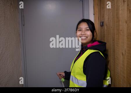 Smiling female blue collar worker standing in front of door Stock Photo