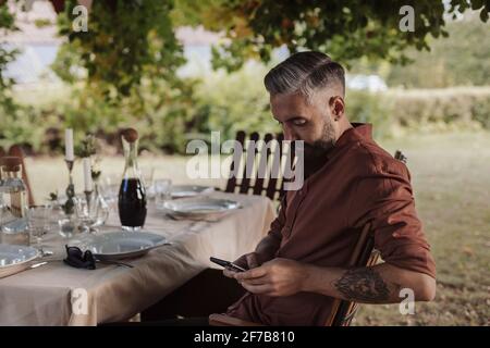 Man sitting at table in garden and using cell phone Stock Photo
