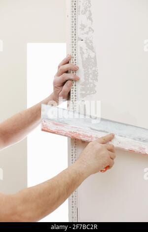 Builder in protective mask using a trowel to add plaster. Plastering wall with putty-knife, close up image. Fixing wall surface and preparation for pa Stock Photo