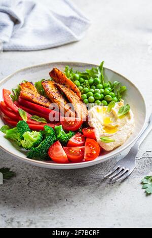 Vegan salad bowl with sweet potatoes, broccoli, tomato, peas and hummus. Healthy food concept. Stock Photo