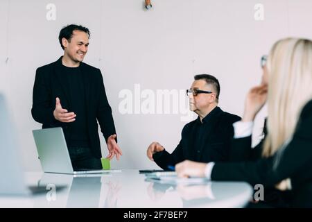 Group of young modern people in smart casual wear discussing business and smiling while sitting in the creative office Stock Photo