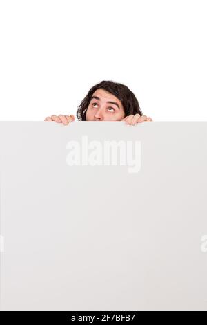 Fearful and doubtful man, hiding behind a blank whiteboard, looking up suspicious and afraid. Empty sheet with copy space for advertising and messages Stock Photo