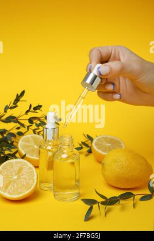 Female hand dripping lemon essential oil from a pipette on a yellow background with lemon slices, natural cosmetics concept Stock Photo