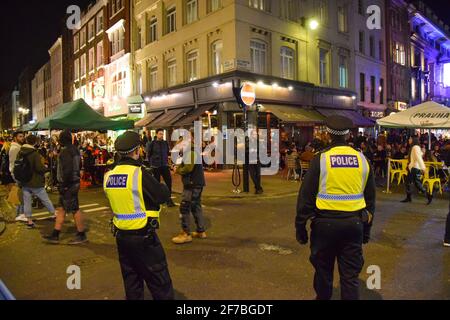 Police officers and crowd of people on Old Compton Street, Soho at night. Temporary al fresco street seating was implemented to allow bars and restaurants to operate and facilitate social distancing during the coronavirus pandemic. London, United Kingdom, 4th November 2020. Stock Photo