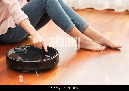 Faceless middle section of young woman using automatic vacuum cleaner to clean the floor, controlling smart machine housework robot Stock Photo