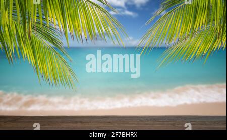 Wooden table and palm leaves in front of blurred tropical sea background. Stock Photo