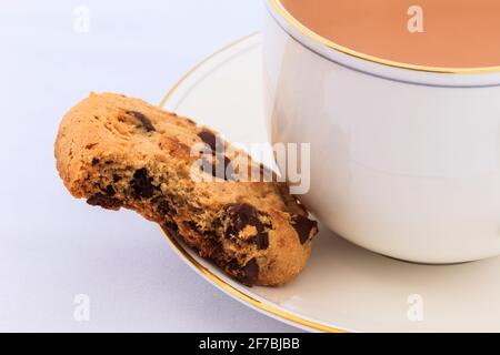 Cup of English tea and a chocolate chip biscuit with a bite taken out on the saucer. Stock Photo