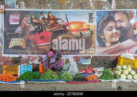 Rayagada, India - February 2021: A woman selling vegetables next to Bollywood movie posters in the Rayagada market on February 16, 2021 in Odisha Stock Photo