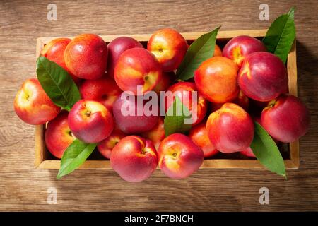 fresh ripe nectarines with leaves in a wooden box, top view Stock Photo