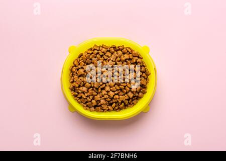 dry cat food in yellow plastic bowl isolated on pink background Top view flat lay Delicious treat for your beloved pet Food for animals concept Stock Photo