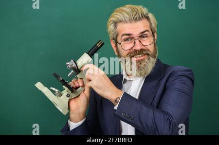 School teacher looking microscope. Scientific research. Fascinating research. Teacher with microscope. Man hipster classroom chalkboard background Stock Photo