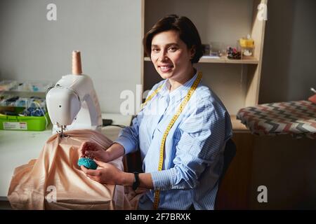 Seamstress with tape measure removing pin from cushion Stock Photo