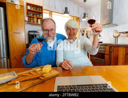 COVID-19 Stay connected and hope concept. Happy senior couple with wine video calling friends on laptop or online chatting with family celebrating eas