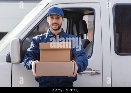 young arabian postman holding parcels and looking at camera near car Stock Photo
