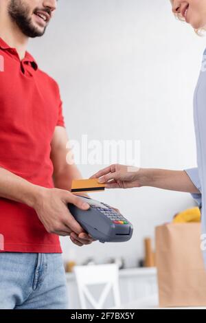 partial view of smiling delivery man holding payment terminal near woman with credit card Stock Photo