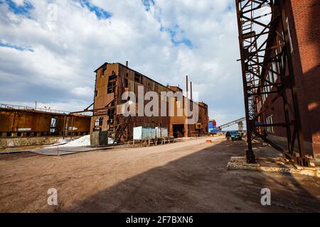 Demolition of outdated Soviet sulfuric acid plant. Outside view on rusted industrial building. Blue sky with clouds. Stock Photo