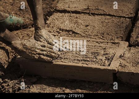 A worker making sustainable mud bricks to construct a greenhouse to ...