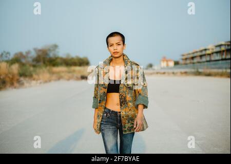 Young short hair Asian woman wearing sports bra and army jacket, walking straight towards the camera with confidence and determination. Stock Photo