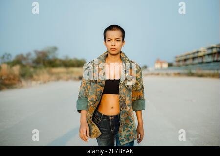 Young short hair Asian woman wearing sports bra and army jacket, walking straight towards the camera with confidence and determination. Stock Photo