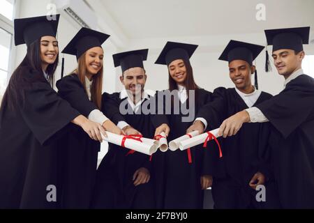Happy smiling multiracial graduates stack their diplomas together standing in class. Stock Photo