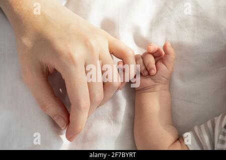 Mother Baby Connection. Newborn child holding mom's hand while lying in bed