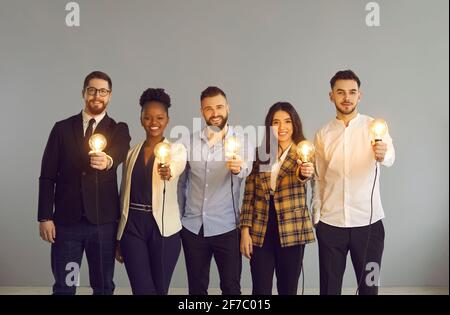Diverse business team holding light idea bulb stand over grey studio background Stock Photo