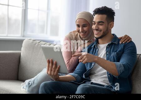 Cheerful arab guy showing something girlfriend on Internet, using pad Stock Photo