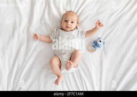 Adorable newborn baby wearing bodysuit lying on bed and looking at camera Stock Photo
